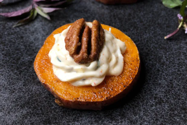 Roasted sweet potato round topped with a swirl of cream and a toasted pecan half